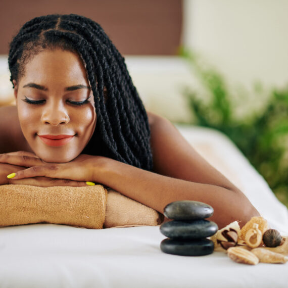 Smiling young Black woman lying on bed in spa salon with eyes closed after getting rejuvenating treatment