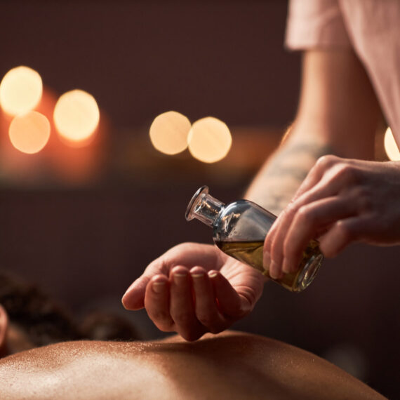 Hands of spa therapist applying massage oil on back of client